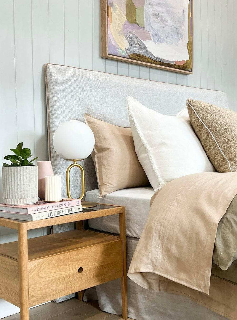 Ethnicraft Spindle Bedside table in natural oak with single drawer and smokey glass top next to bed with beige and white pillows