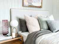 norsu Studio Cushion in celadon green with white leather piping on a bed with mixed textured cushions