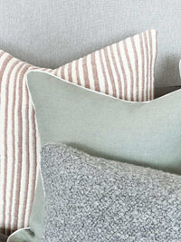 norsu Studio Cushion in haven celadon with white leather piping displayed on a sofa with textured and striped cushions