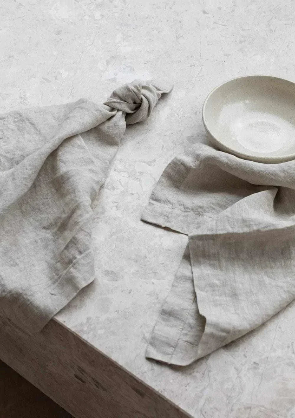 Set of four natural Rendr 100 linen napkins made from 100% prewashed European flax with 3cm hem on a textured surface next to a beige bowl