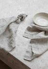 Set of four natural Rendr 100 linen napkins made from 100% prewashed European flax with 3cm hem on a textured surface next to a beige bowl