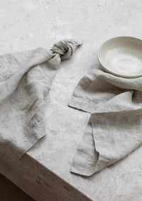 Set of four natural Rendr 100 linen napkins made from 100% prewashed European flax with 3cm hem on a textured surface next to a beige bowl