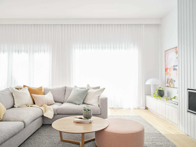Bright modern living room with grey sectional sofa adorned with norsu Studio Cushion in neutral tones, round wooden coffee table, and soft natural light from large windows