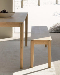 Ethnicraft Bok Bench in natural oak wood with minimalist design placed next to a dining table in a bright indoor setting