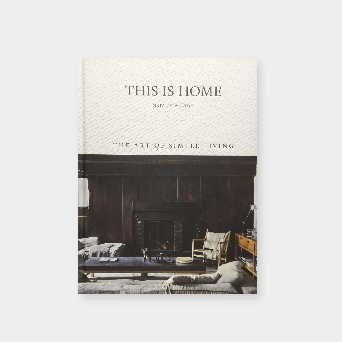 Book cover of "This Is Home: The Art of Simple Living" by Natalie Walton featuring a cozy living room with a fireplace and neutral decor.