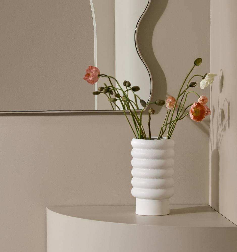 White Alder Pot with textured bubbly matte exterior and gloss interior holding delicate flowers on a curved beige surface