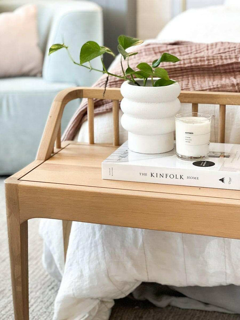 White Alder Pot with textured bubbly finish holding a green plant on a wooden bedside table next to a candle and book