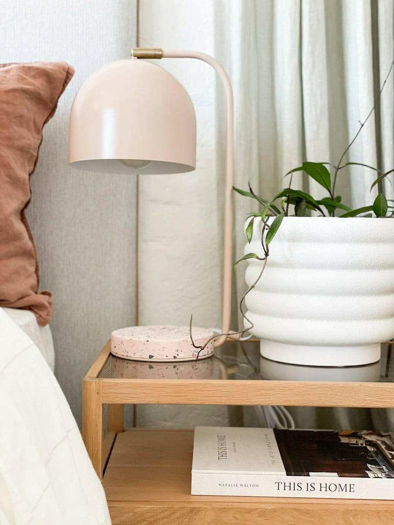 White porcelain Alder Pot with textured bubbly finish on a wooden bedside table next to a beige lamp and plants