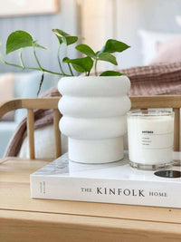 White textured bubbly Alder Pot planter with green plant on a wooden table next to a candle and book