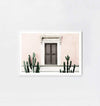 Middle of Nowhere blush villa framed print with pink wall, brown shuttered window, and green cacti in white frame