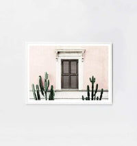 Middle of Nowhere blush villa framed print with pink wall, brown shuttered window, and green cacti in white frame