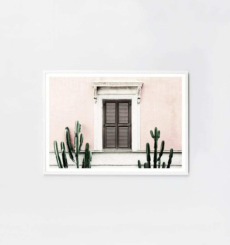 Middle of Nowhere blush villa framed print with pink wall, brown shuttered window, and green cacti in white frame