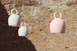 POTT Lighting Calo Pendant lamps in white and salmon, handmade ceramic bell-shaped pendants with natural rope, hanging against a textured stone wall.