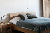 Ethnicraft Azur bedside table in natural oak with one drawer beside wooden bed with gray bedding and pillows in a minimalist bedroom