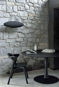 Black Ethnicraft Bok Dining Chair made of solid European oak with sculptural contemporary design in a rustic stone-walled dining setting
