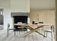 Ethnicraft Mikado Oval Dining Table in natural oak with crossed leg design and modern chairs in minimalist dining room.