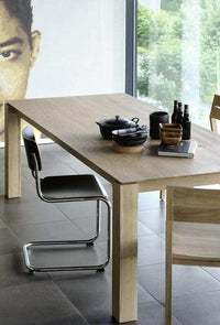Ethnicraft Dining Table Slice made of natural oak with modern chairs in a bright dining room.