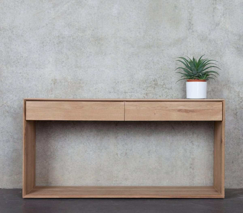 Ethnicraft Nordic Console in natural oak with two drawers against a grey textured wall with a small potted plant on top