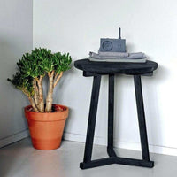 Black Ethnicraft Tripod side table made of solid oak next to a potted plant