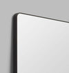 Flynn Curve Leaner Mirror with black frame and rounded corners against gray wall