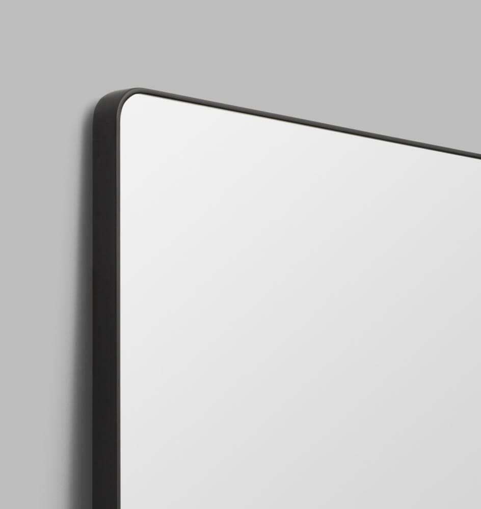 Flynn Curve Leaner Mirror with black frame and rounded corners against gray wall