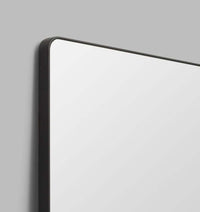 Flynn Curve Leaner Mirror with black frame and rounded corners against gray wall