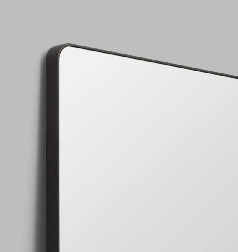 Flynn Curve Leaner Mirror with black frame and rounded corners against gray wall