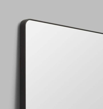 Flynn Curve Leaner Mirror with black frame and rounded corners against gray wall