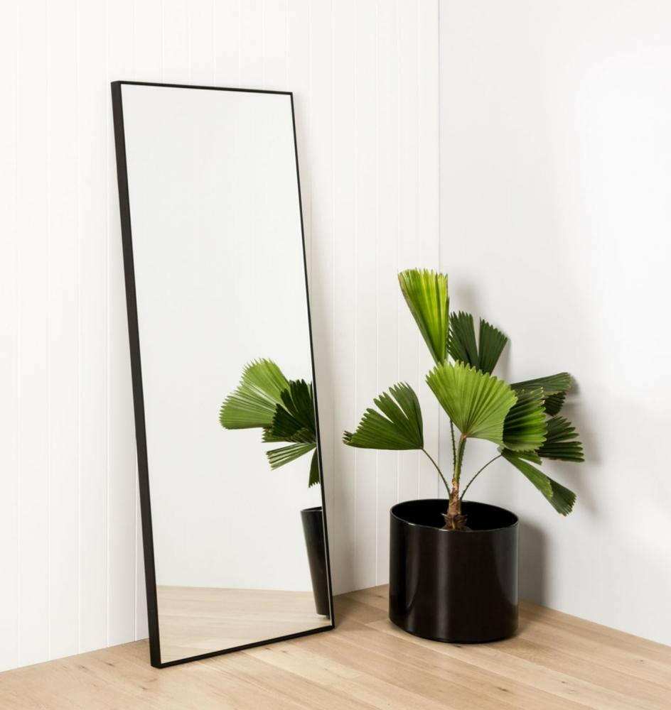 Middle of Nowhere Flynn Leaner Mirror in black with minimalist wooden frame leaning against white wall next to potted green plant