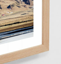 Framed Middle of Nowhere photographic print featuring a small Icelandic town beneath a glacier with oak frame