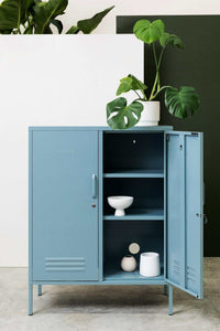Blue Mustard Made Locker The Midi Ocean with open door, adjustable shelves, and decorative items inside, set against a white and green background with plants on top.