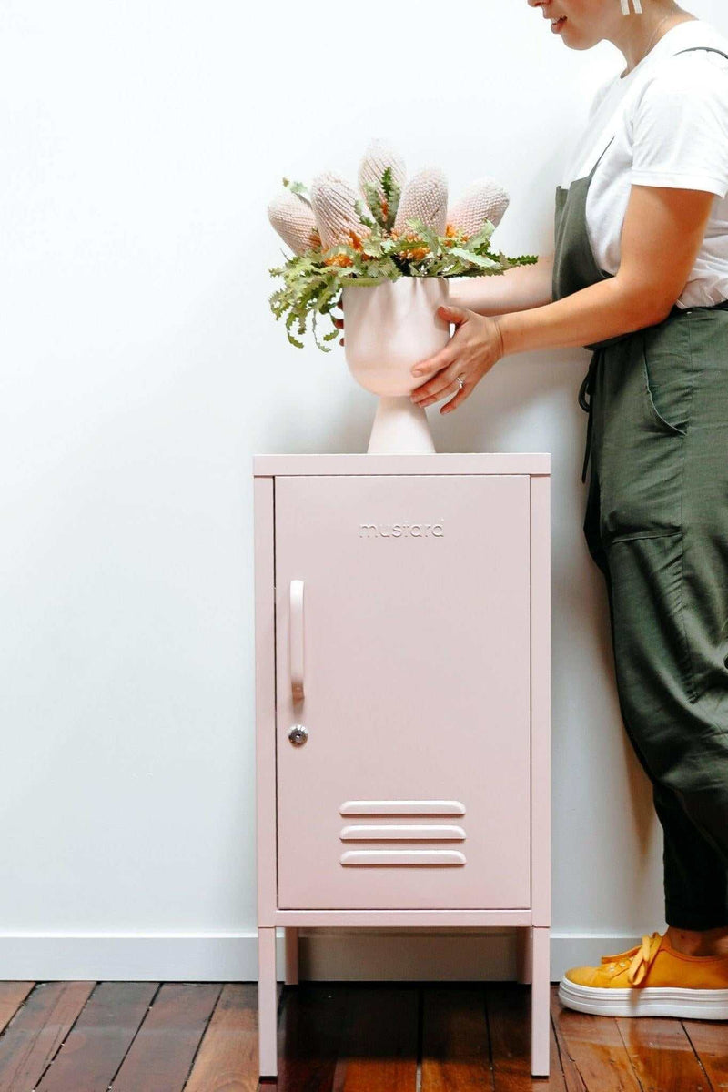 Pink Mustard Made Locker The Shorty Blush with handle, lock, and air vents standing on wooden floor next to person arranging flowers