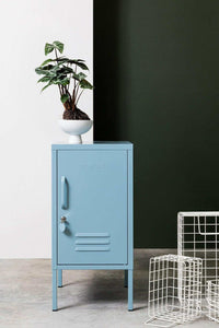Blue Mustard Made Locker The Shorty Ocean with handle, lock, and ventilation vents standing next to a green wall and wire baskets.