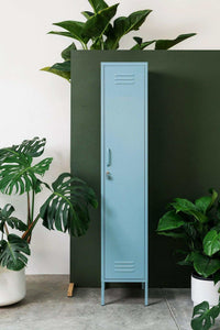 Slim blue Mustard Made Locker "The Skinny Ocean" standing against dark green wall with plants around
