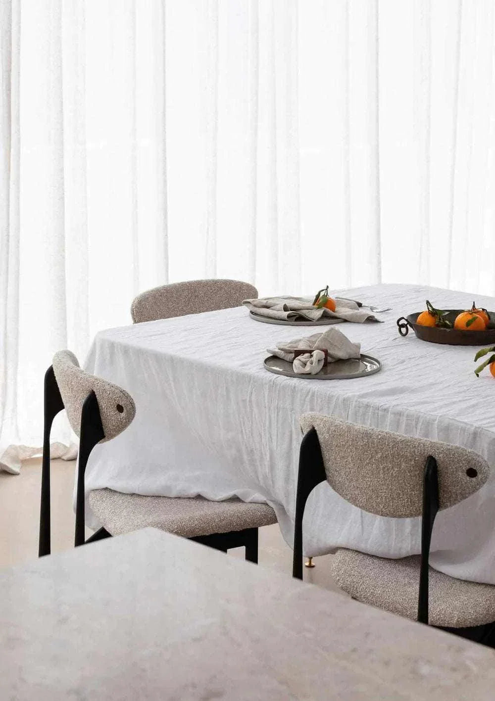 Set of four Rendr 100 Linen Napkins in natural color on a white linen tablecloth with modern dining chairs