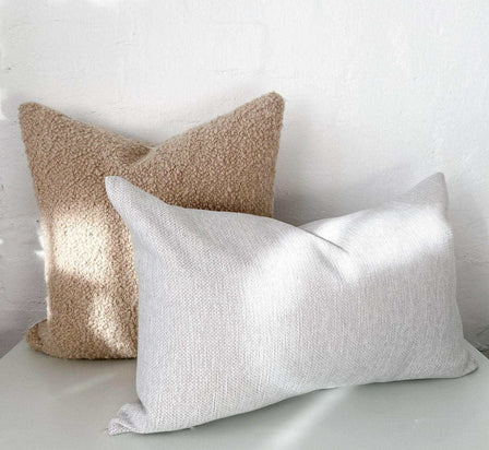 norsu Studio Bouclé Buff cushion with white leather piping and textured neutral throw pillows on white surface