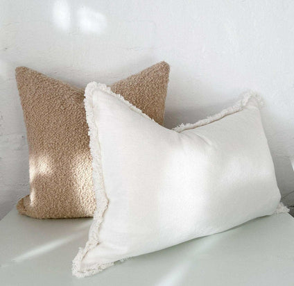 norsu Studio Bouclé Buff cushion with white leather piping and plush feather-down filling displayed in neutral tones