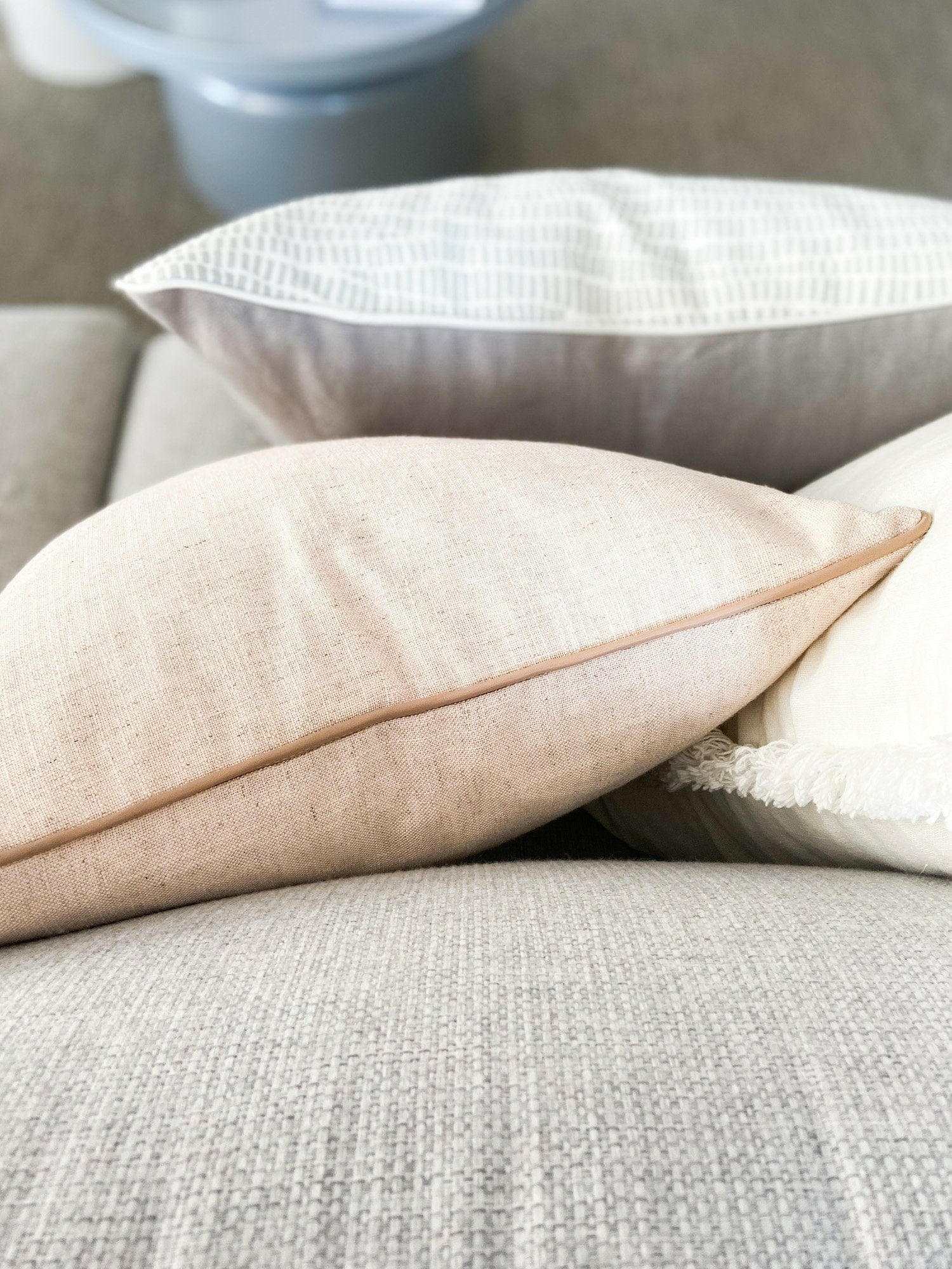 norsu Studio Cushion Lexus Rosewater with blush leather piping on grey sofa