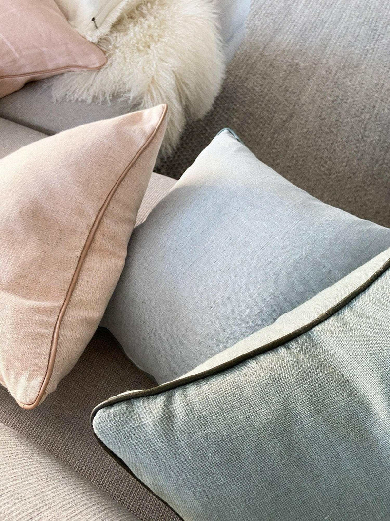 Handmade norsu cushion in Lexus Seaglass with olive leather piping on a sofa with other cushions