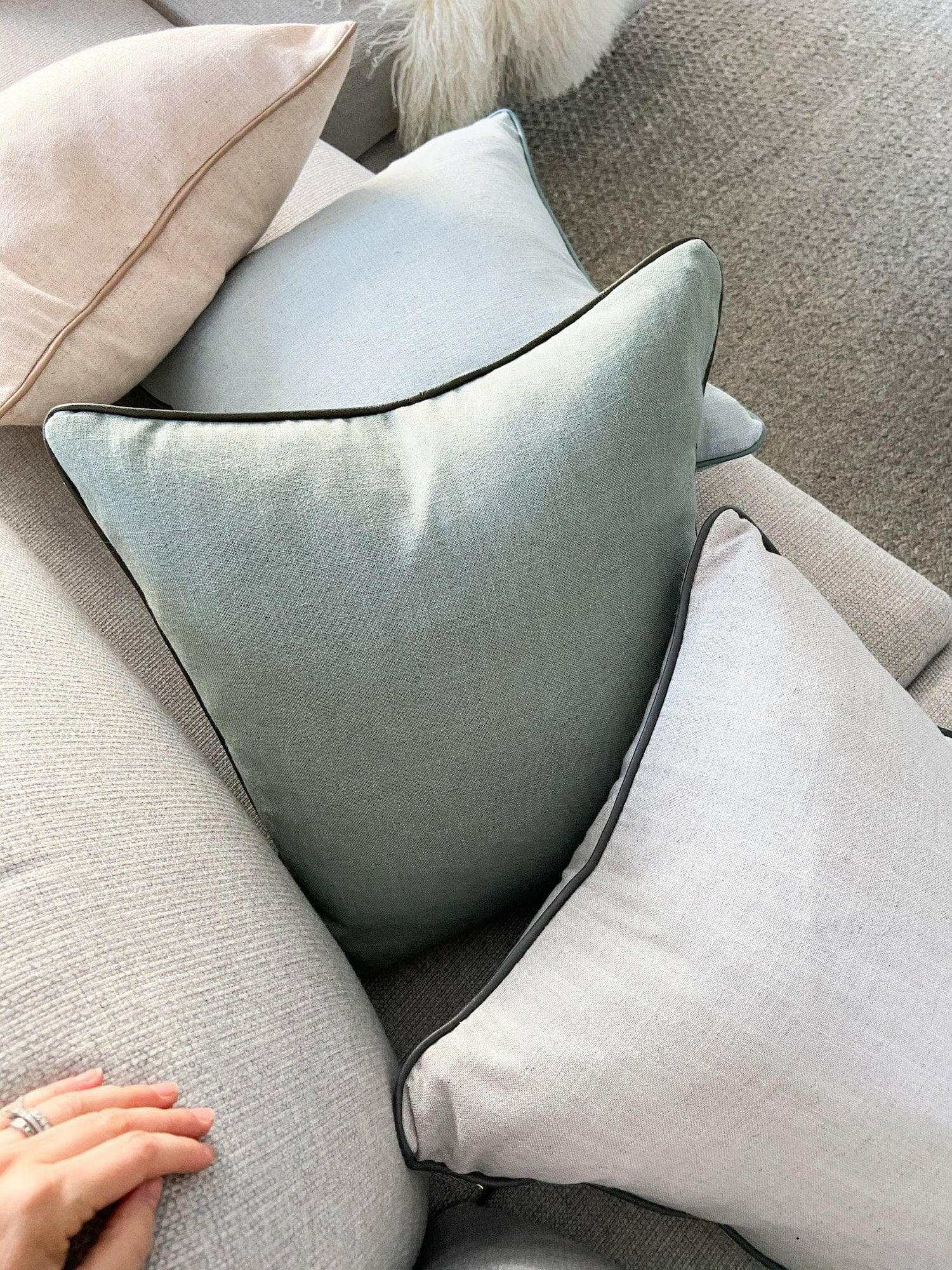 Handmade norsu cushion in Lexus Seaglass fabric with olive leather piping on a beige sofa