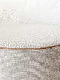 Round norsu Ottoman in Lindeman Snow fabric with blush leather piping, soft foam-filled, available in various sizes.