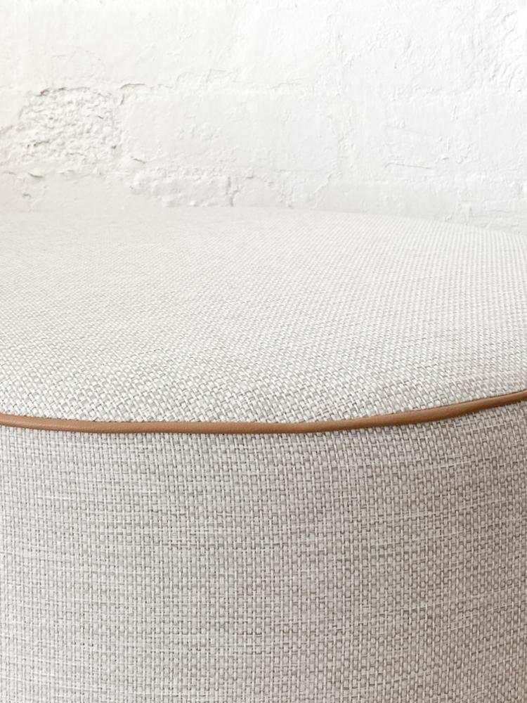 Round norsu Ottoman in Lindeman Snow fabric with blush leather piping, soft foam-filled, available in various sizes.
