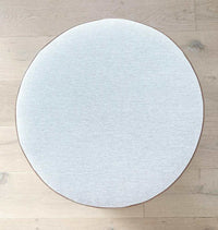 Round norsu Ottoman in Lindeman Snow fabric with blush leather piping on wooden floor