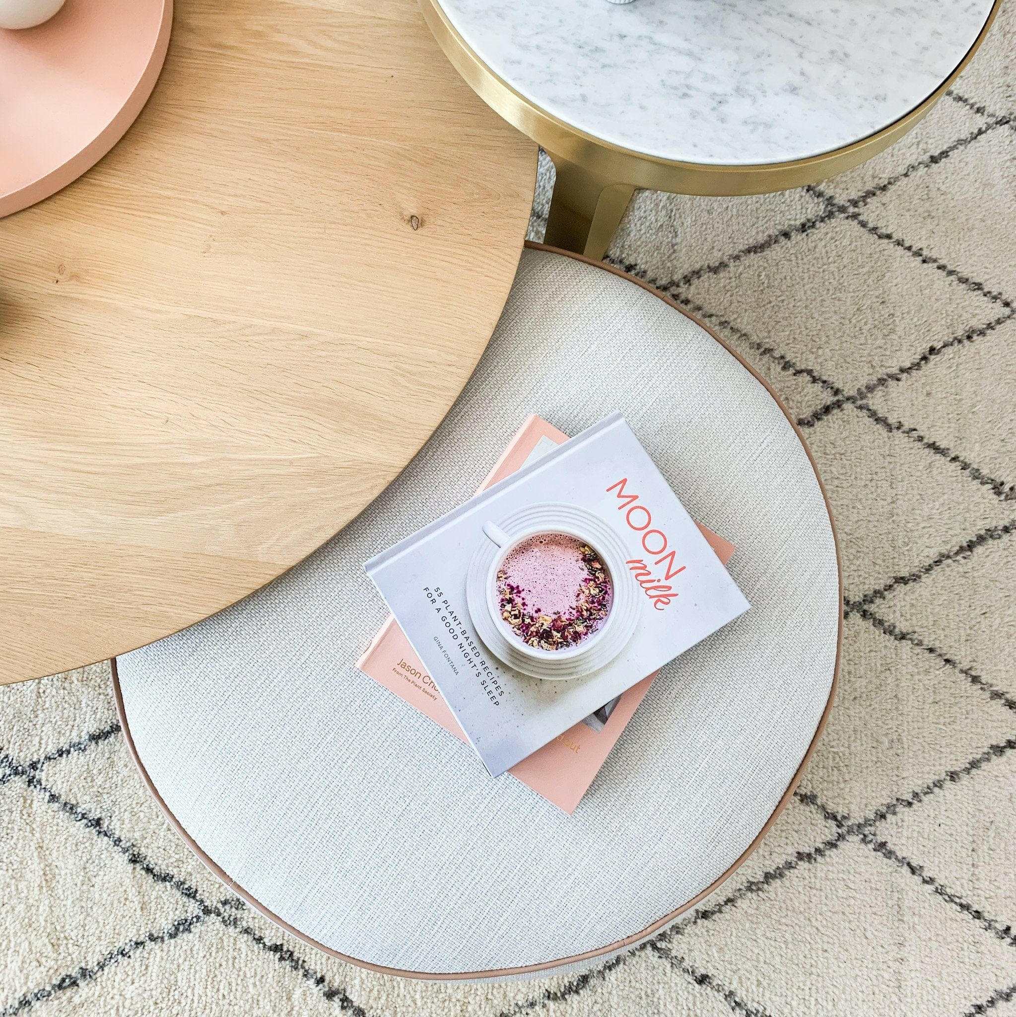 norsu Ottoman in Lindeman Snow fabric with blush leather piping, round soft ottoman with books on top on patterned carpet