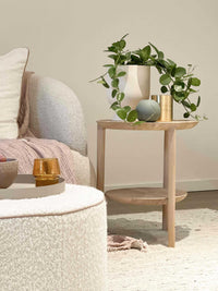 Ethnicraft Oak Bok Side Table with minimalist design featuring a round top and lower shelf, styled with a potted trailing plant and decorative items in a cozy living room setting.