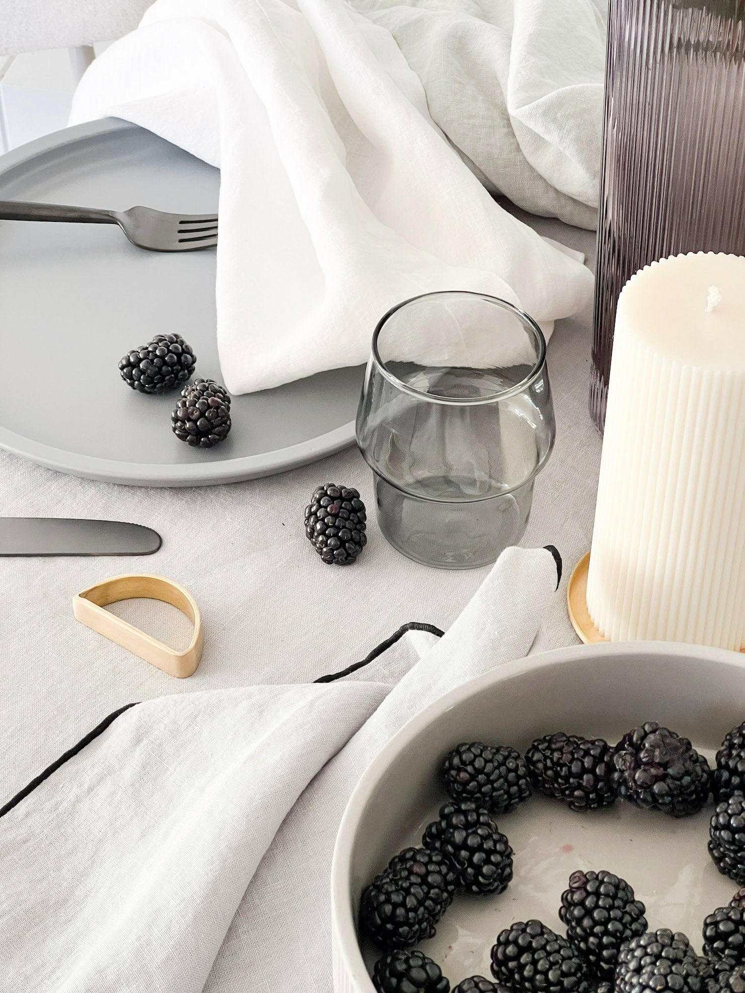 Set of four white Rendr 100% linen napkins on a dining table with blackberries, glass, candle, and plate.