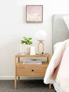Brass desk lamp with frosted glass shade on wooden bedside table next to bed in modern bedroom setting