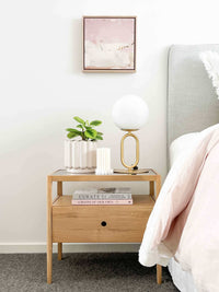 Brass desk lamp with frosted glass shade on wooden bedside table next to bed in modern bedroom setting