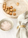 Set of four Rendr 100% linen natural napkins with a gold napkin ring beside dried figs and a bowl of pink salt on a marble tray