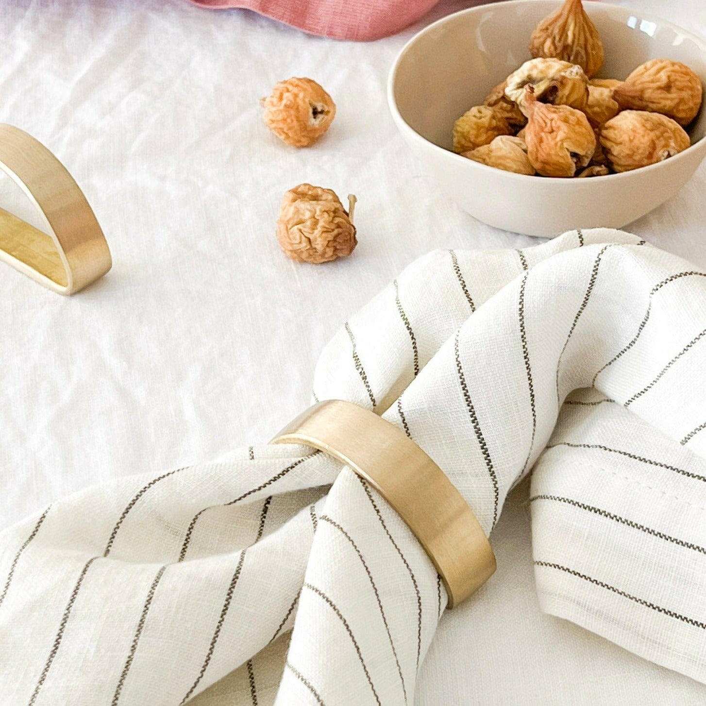 Set of four Rendr 100% linen striped olive napkins with gold napkin rings on white tablecloth